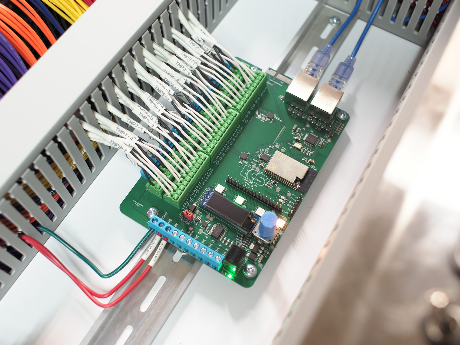 TMUX30-SS board installed in a panel, with labeled thermistor wiring on green terminals, two Ethernet cables, an OLED display, and blue control-line terminals